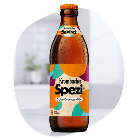 Braune Glasflasche mit orangefarbenem Verschluss und Etikett "Krombacher Spezi Cola-Orange-Mix" mit buntem Muster.