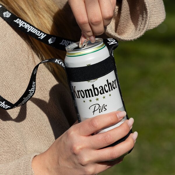 Hand zieht Lasche an einer Krombacher Pils Dose in schwarzem Getränkehalter mit Krombacher-Schriftzug.