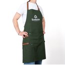 Person trägt grüne Krombacher Grillschürze mit braunen Trägern und Logo auf der Brust, drunter weißes T-Shirt.