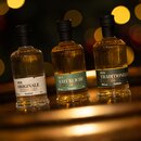 Drei kleine Krombacher Spirituosenflaschen mit schwarzen Verschlüssen, beschriftet mit 'Der Originale', 'Der Natürliche' und 'Der Traditionelle', vor unscharfem Lichthintergrund.