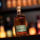 Flasche Krombacher Bierbrand 'Der Natürliche' mit grünem Etikett, 0,5 Liter, 38 % Vol., bernsteinfarbener Inhalt, auf dunklem Untergrund.