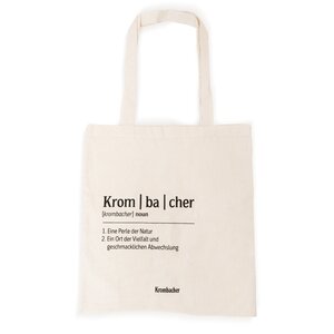 Beiger Jutebeutel mit schwarzem Text in Lautschrift 'Krom|ba|cher' und Definitionen, darunter 'Eine Perle der Natur' und 'Ein Ort der Vielfalt und geschmacklichen Abwechslung', Marke Krombacher.